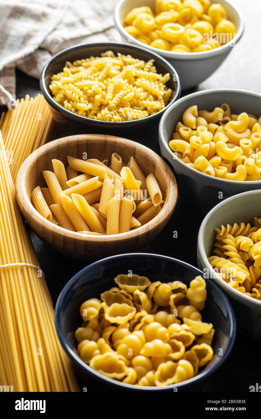 Varios tipos de pasta italiana cruda en cuencos en mesa de cocina. Foto de stock