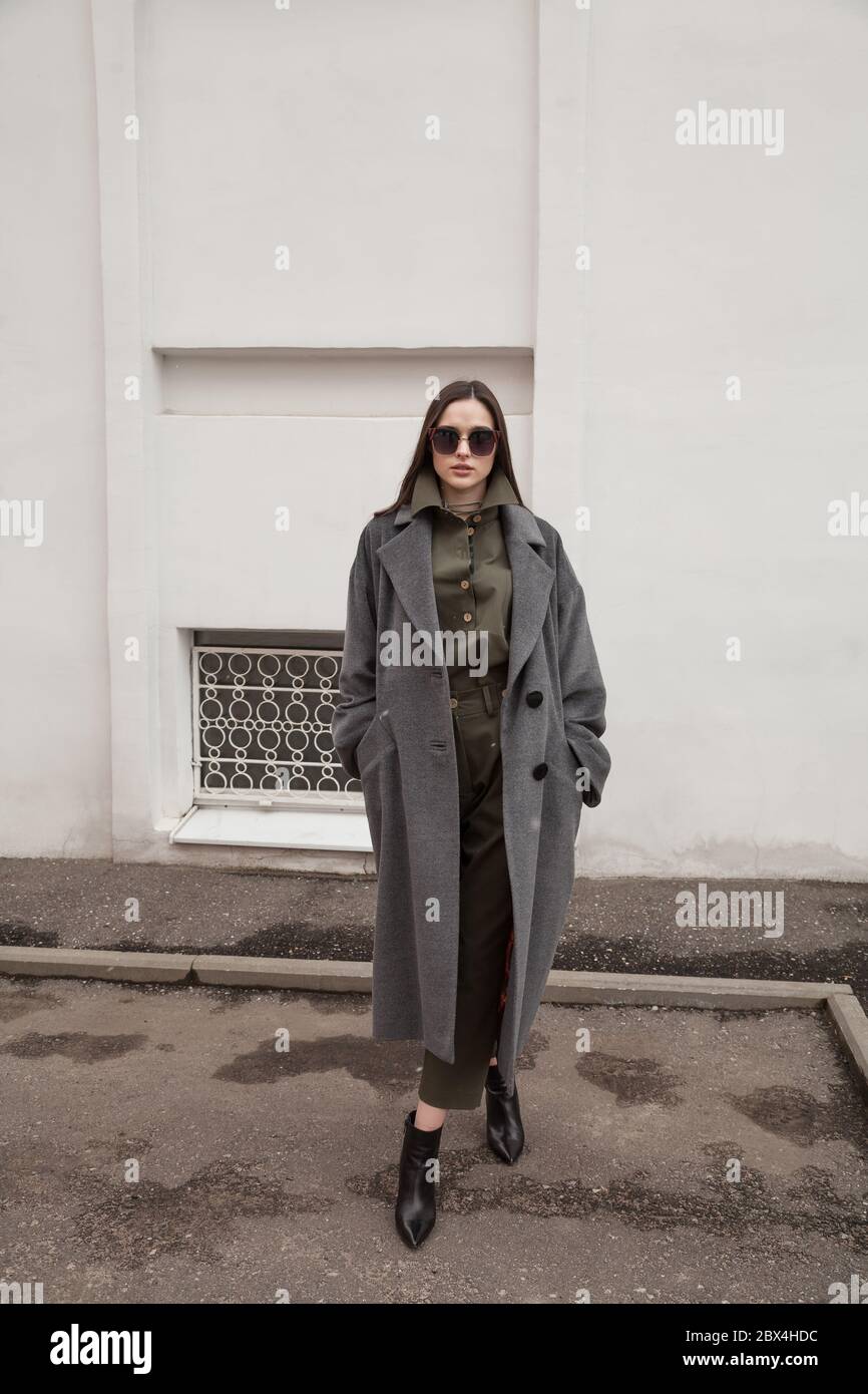 joven mujer morena con estilo con abrigo largo, traje y zapatos, caminando por calles, atractiva mujer en ropa informal de moda y gafas de sol Fotografía de stock - Alamy