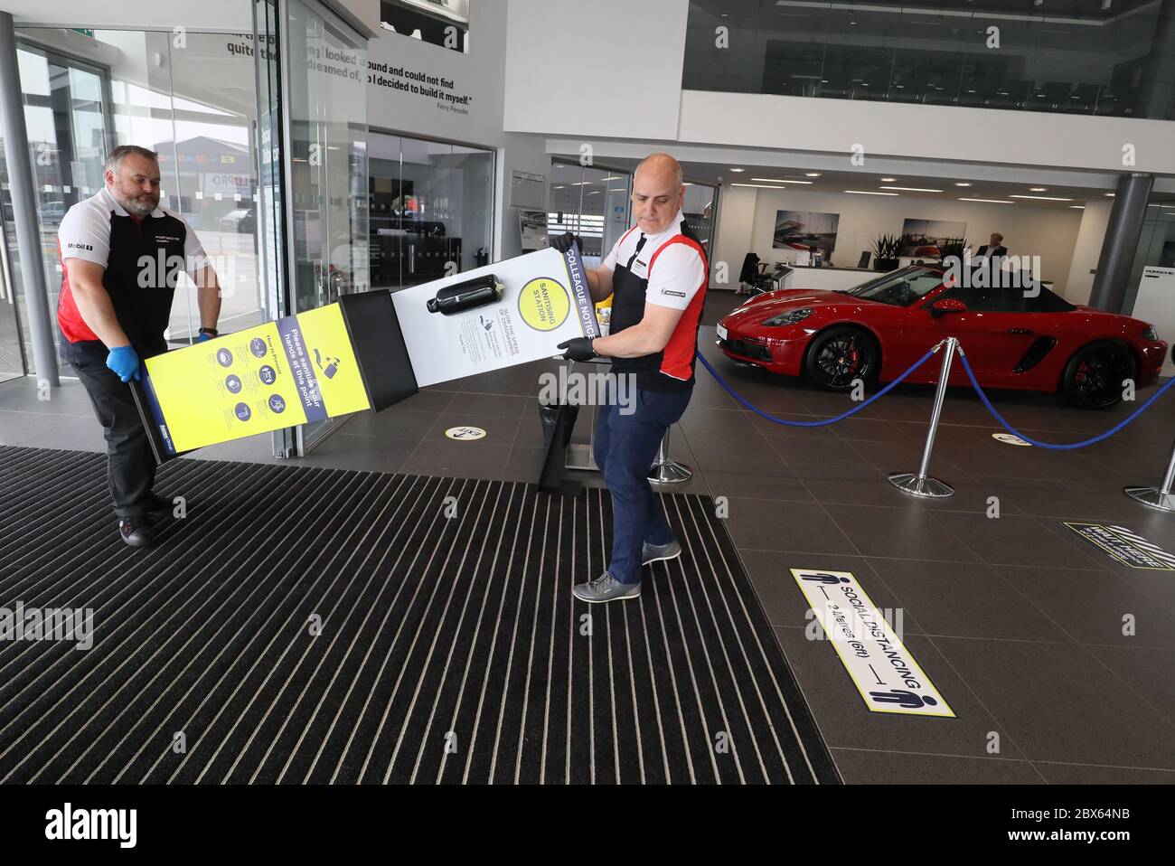 Steven Biggerstaff y George Straghan (derecha) traen un desinfectante de manos al Porsche Center Belfast mientras preparan la sala de exposición de coches para su apertura el lunes, ya que las medidas de bloqueo se están aliviando en la provincia. Foto de stock