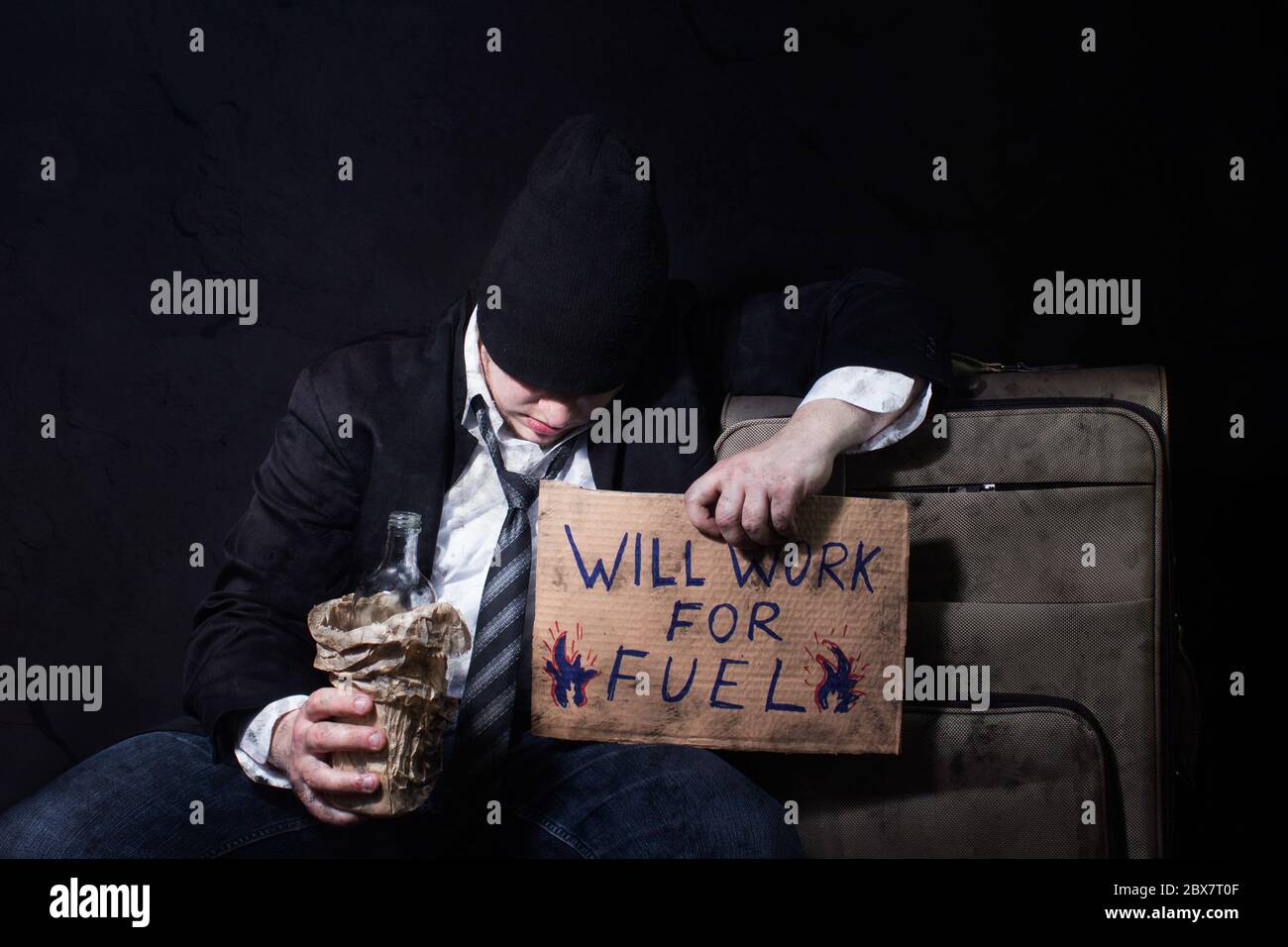 Foto de un hombre de negocios emborrachado sin hogar durmiendo en maleta de viaje con botella vacía y cartel de cartón. Foto de stock