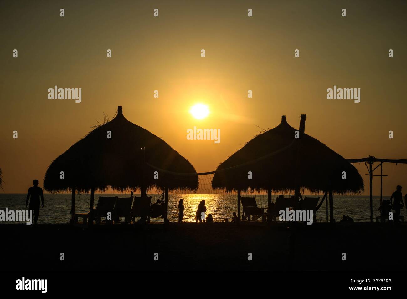 Una vista de la puesta de sol a lo largo de la costa, cabañas, y la gente que disfruta de la vista majestuosa mientras el sol se pone a través del horizonte Foto de stock