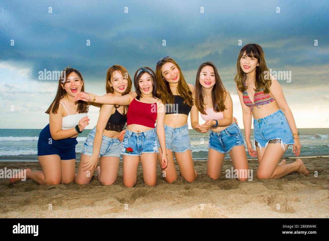retrato de feliz y hermoso grupo de mujeres asiáticas coreanas y chinas,  jóvenes bonitas niñas posando juntas arrodillándose en la playa de arena  sonriendo alegre a Fotografía de stock - Alamy