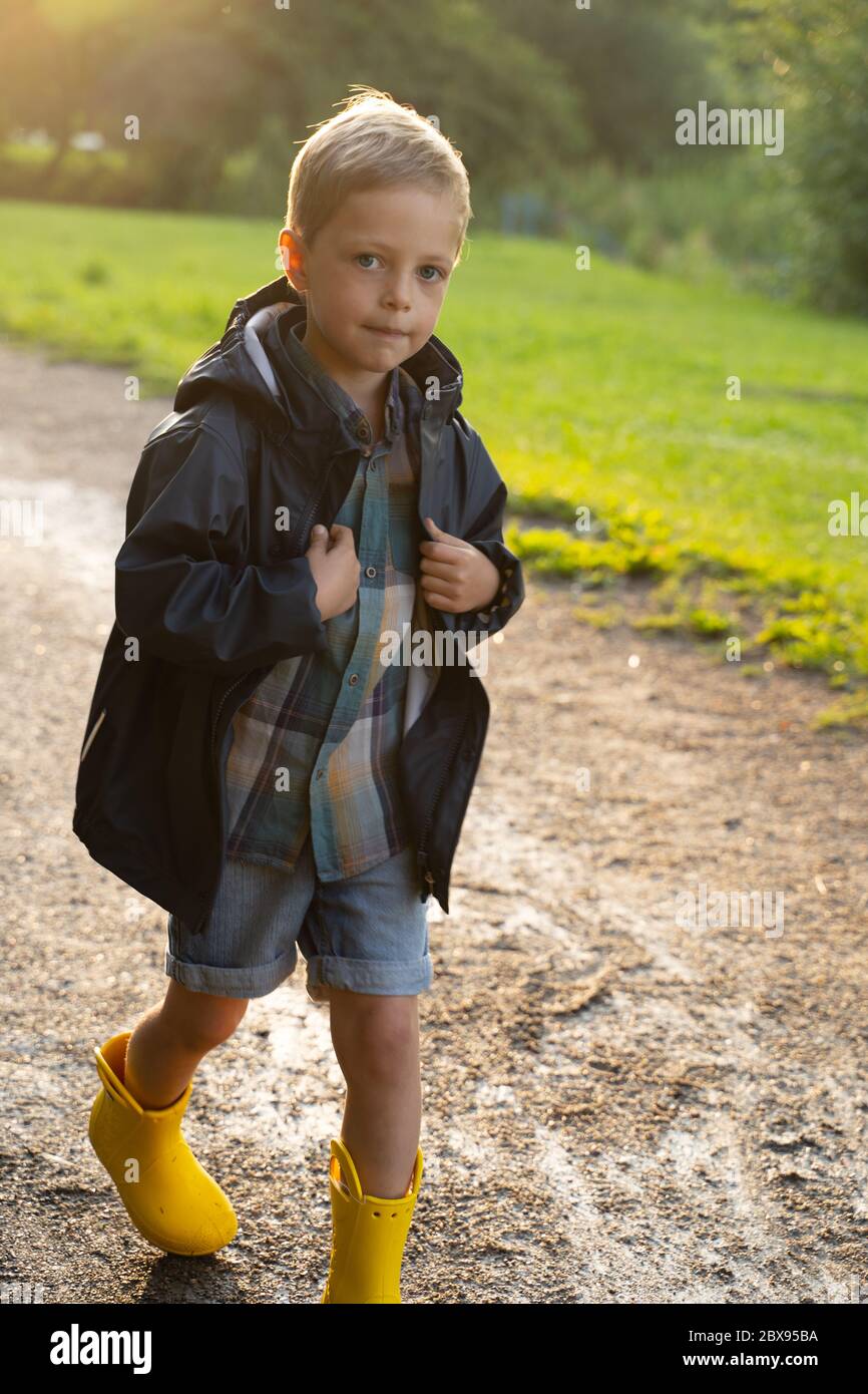 Colgar mental fluido Niño de preescolar con botas amarillas de lluvia caminando en el parque  después de la lluvia. Niño jugando y divertirse en la soleada primavera o  en el día de verano. Juegos al