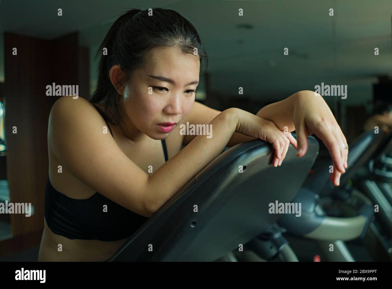 Joven atractiva y en forma de la mujer coreana asiática agotado durante el entrenamiento de carrera en el gimnasio del hotel o gimnasio jogging en la cinta de correr duro con neumático Foto de stock