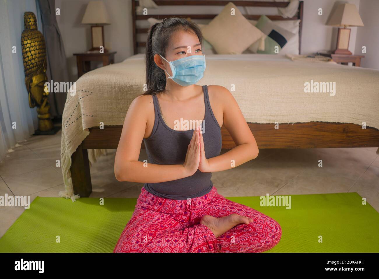 Equilibrio de la mente y el cuerpo durante la cuarentena casera del virus  Covid-19 - joven hermosa y feliz mujer coreana asiática en máscara  protectora haciendo yoga entrenamiento durin Fotografía de stock -