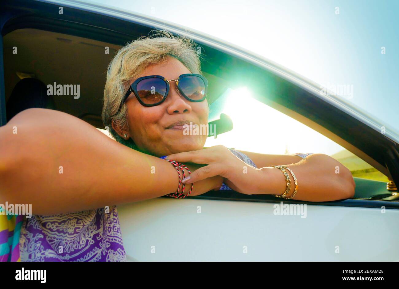 estilo de vida retrato de atractiva y feliz mujer Indonesia asiática de mediana edad 40 o 50 años con pelo gris y hermosa sonrisa sentada en su coche disfrui Foto de stock