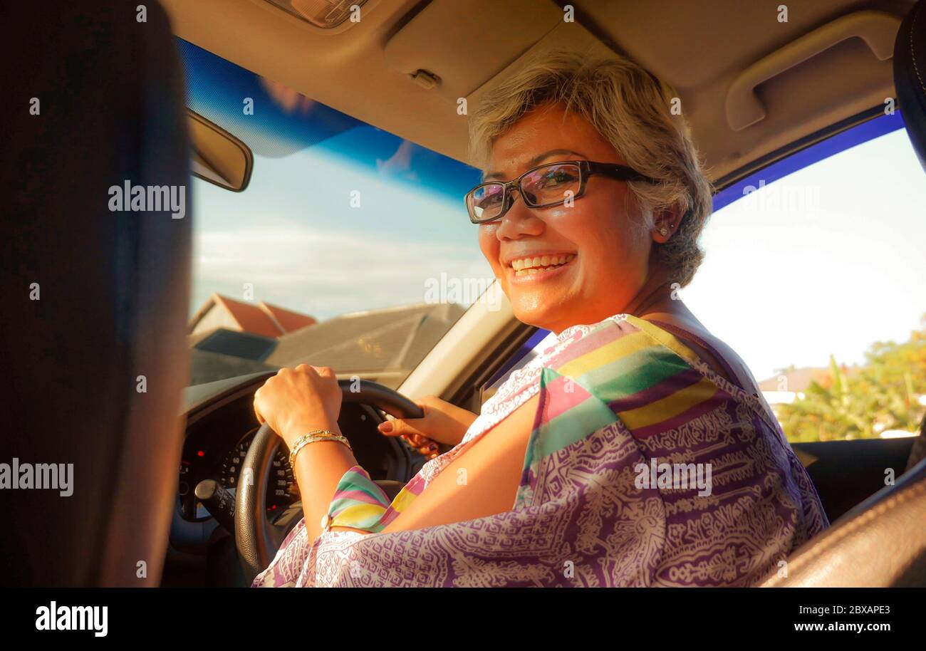 estilo de vida Retrato de verano de mediana edad feliz y atractiva clase asiática Indonesia conducir coche de la mano izquierda sonriendo alegre y libre en un soleado Foto de stock