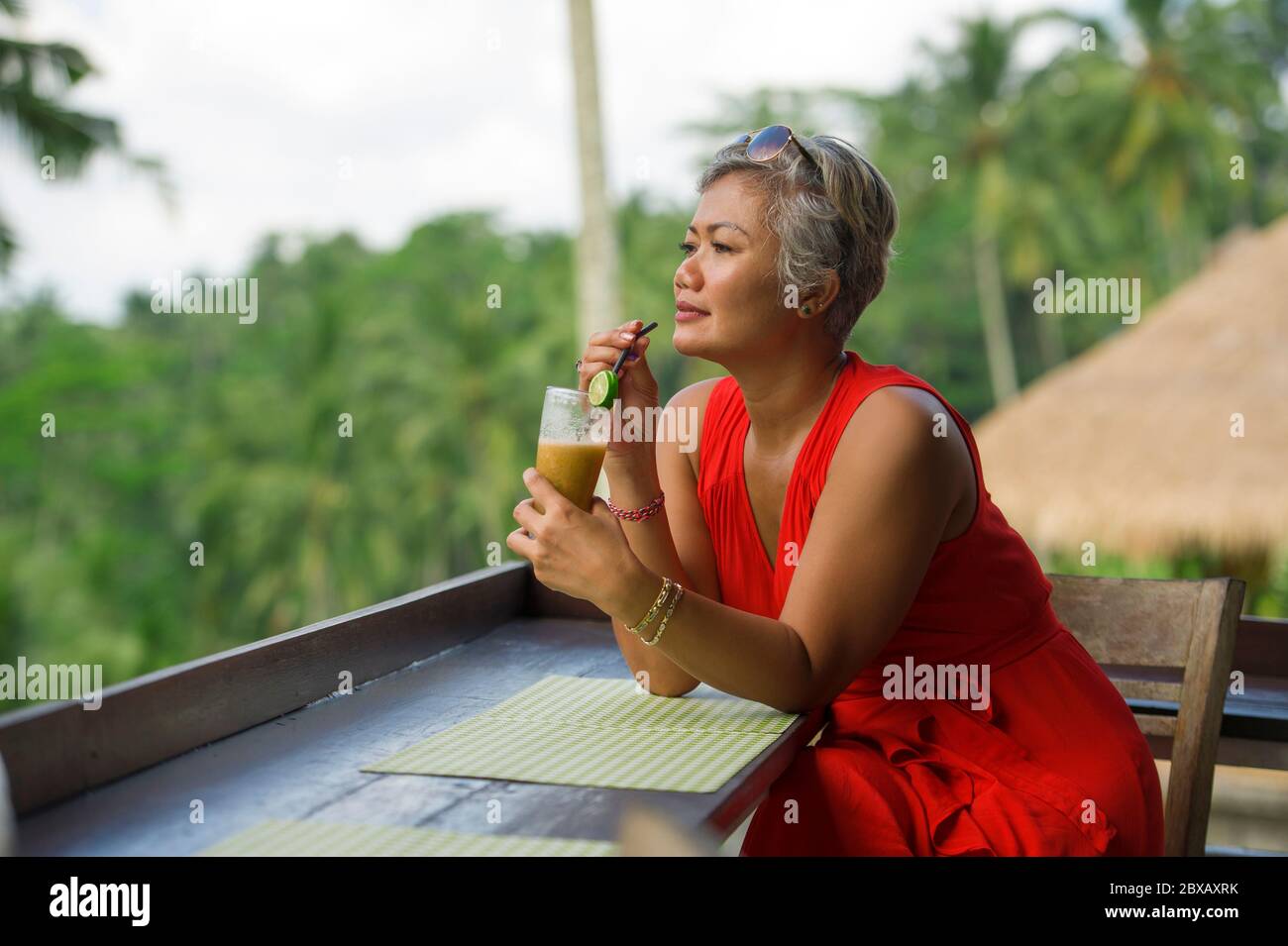 Estilo de vida natural al aire libre retrato de atractiva y feliz mujer Indonesia asiática de mediana edad en elegante vestido rojo disfrutando de un viaje tropical de vacaciones en Foto de stock