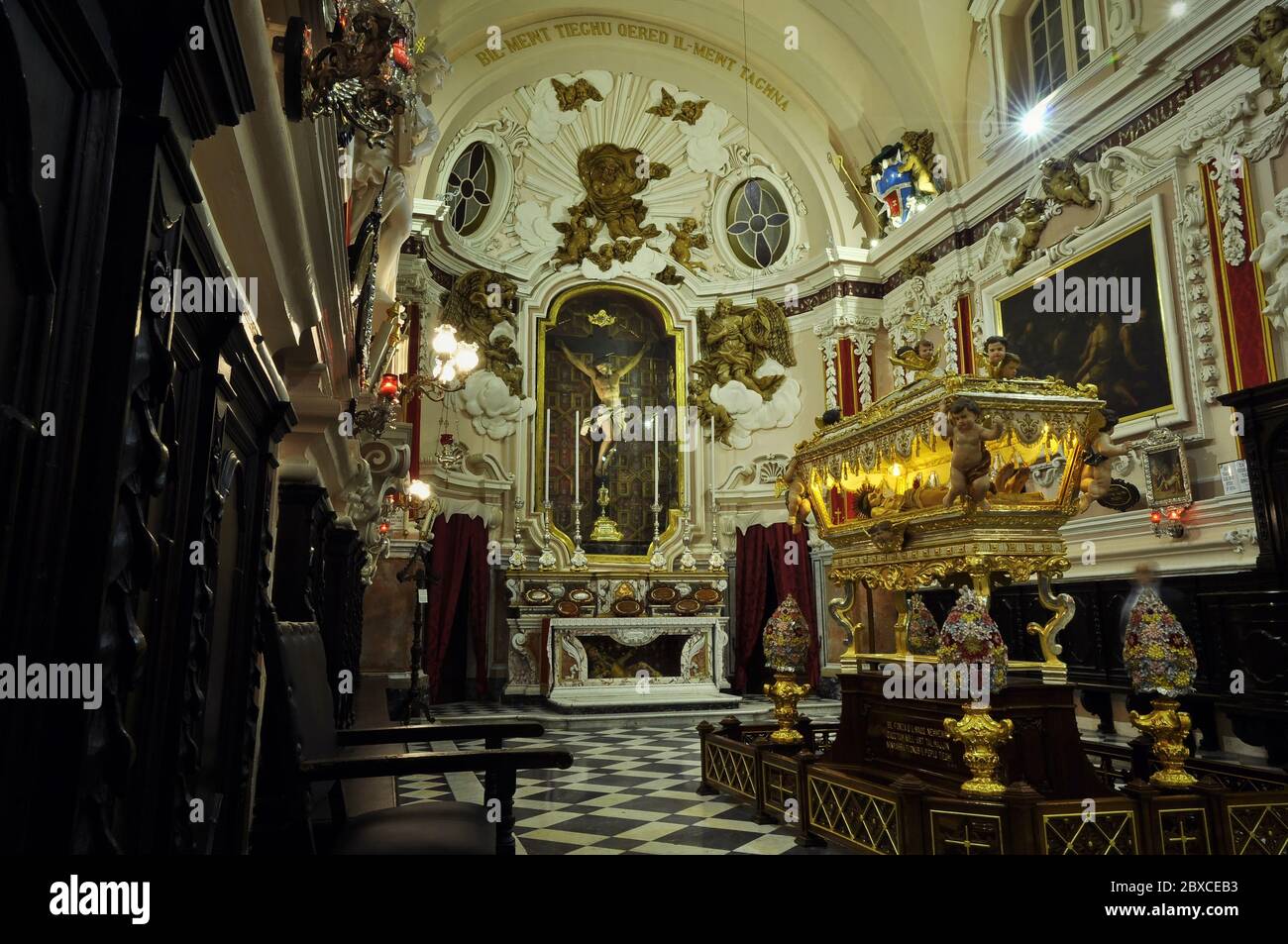 El interior de la capilla lateral de la iglesia barroca, con la tumba simbólica iluminada de Jesucristo en el centro-derecha. Foto de stock