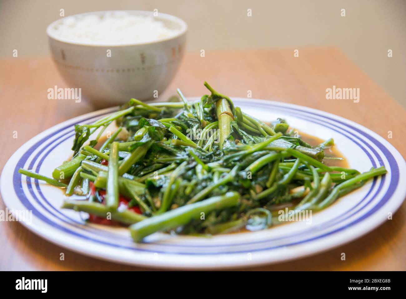 Vista superior de 'Pad Pak Boong', un plato tradicional tailandés: Verduras 'Morning Glory' fritas (Ipomoea aquatica) servidas en un plato blanco Foto de stock