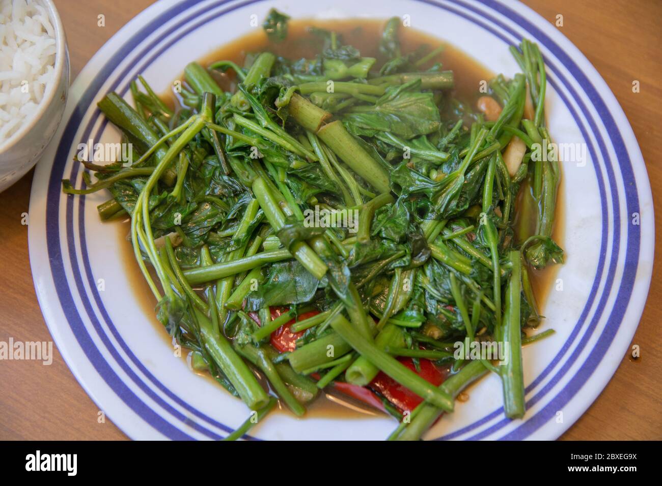 Vista superior de 'Pad Pak Boong', un plato tradicional tailandés: Verduras 'Morning Glory' fritas (Ipomoea aquatica) servidas en un plato blanco Foto de stock