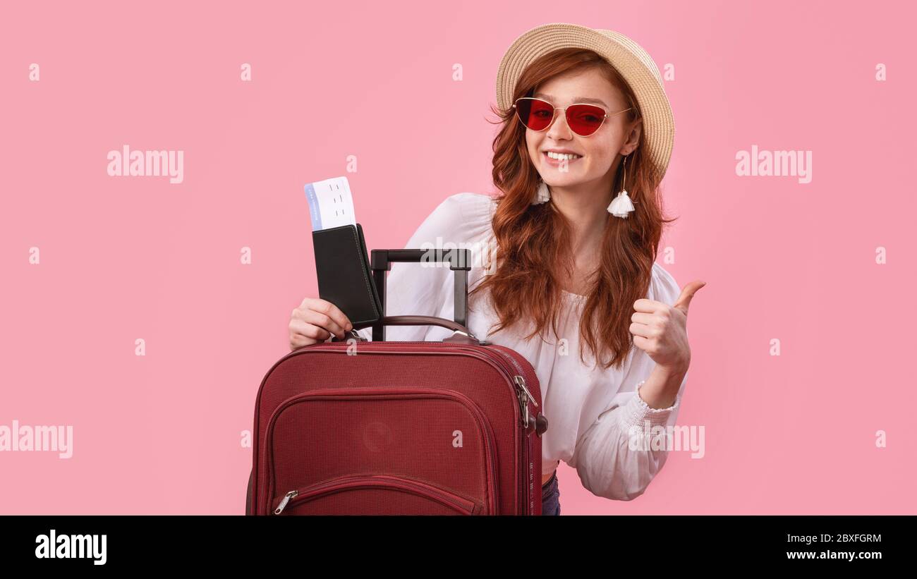 Chica posando con entradas y pasaporte gestuando Thumbs-Up, fondo rosa Foto de stock