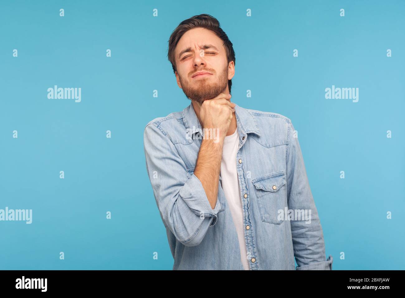 Retrato de un hombre enfermo de gripe en camisa de denim que se atasca el cuello sintiendo mal, sufriendo dolor de garganta y amígdalas inflamadas, dolor insoportable difícil de tragar Foto de stock