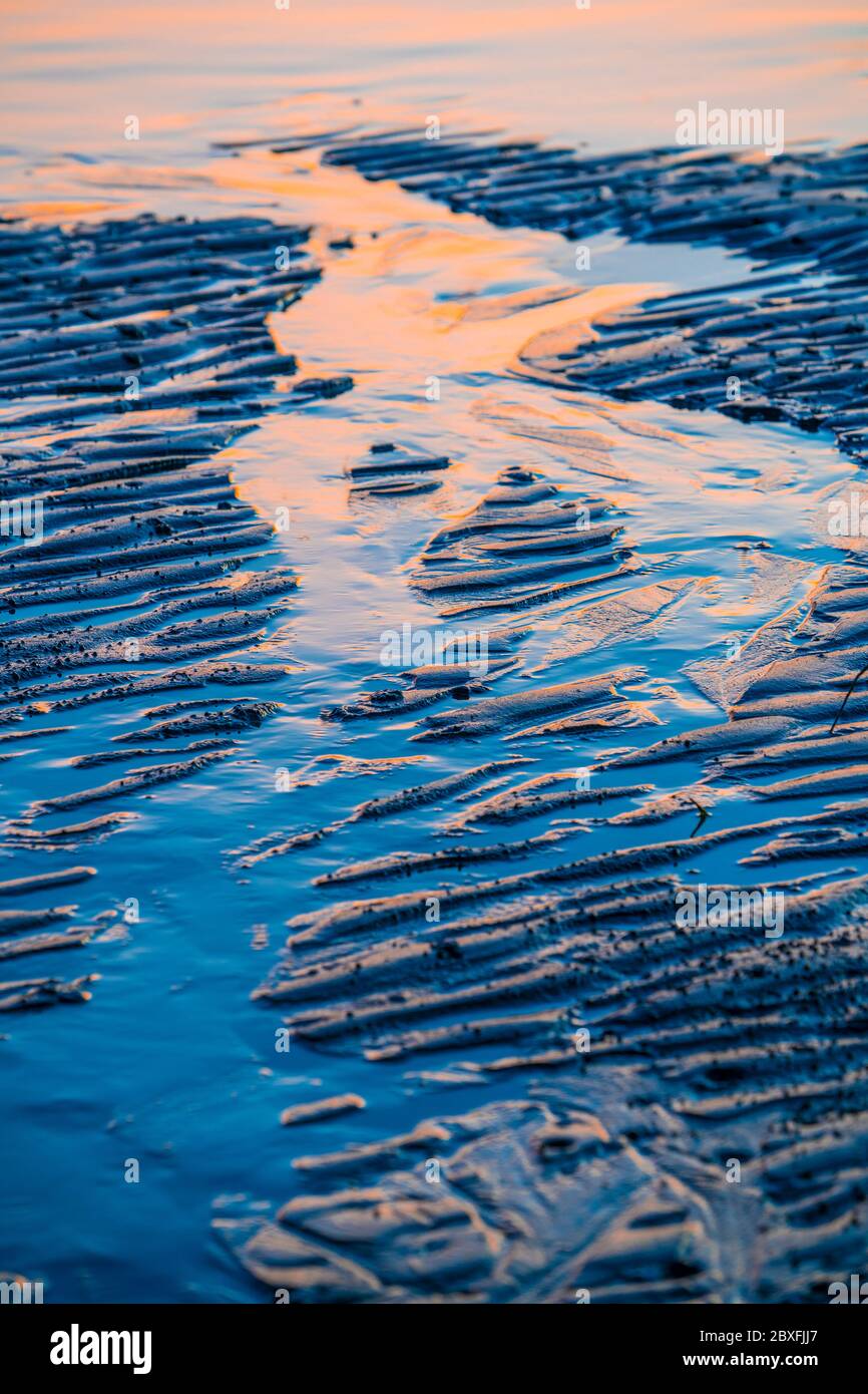 Ondulaciones y reflexiones sobre la arena húmeda de la playa a primera hora de la mañana Foto de stock