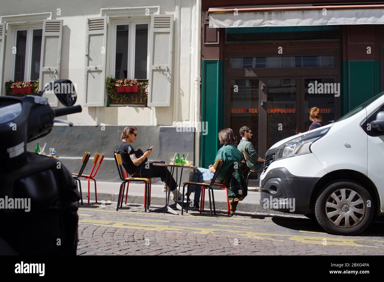 La gente disfruta de una bebida en una terraza de café temporal, entre coches aparcados, en la vida después del encierro - Rue Muller, Montmartre 75018 París, Francia Foto de stock