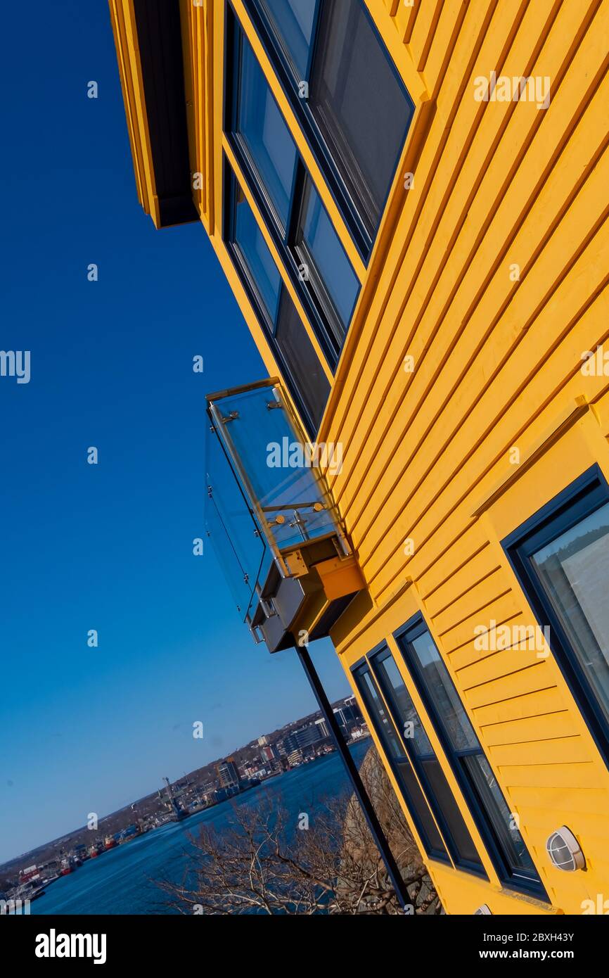 La pared exterior lateral de un edificio de madera de color amarillo brillante con ventanas cerradas y un patio de cristal. El cielo azul brillante está en el fondo. Foto de stock
