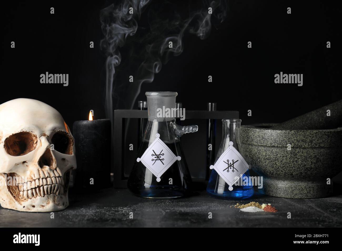 Pociones, cráneo humano, mortero y pedrería en la mesa del alquimista Foto de stock