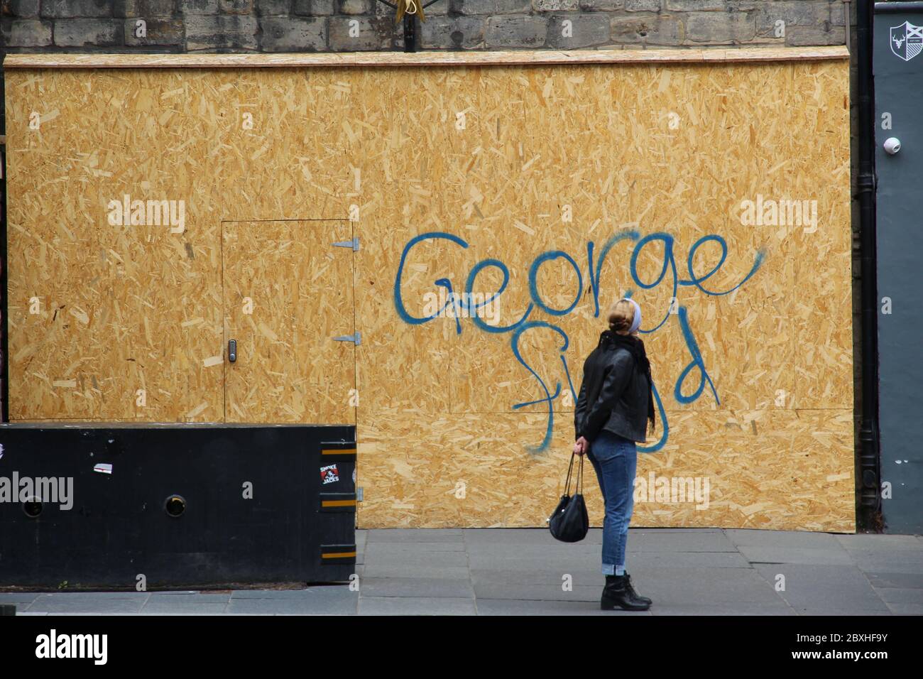 Mujer de pie en la calle mirando el nombre George Floyd escrito fuera de una tienda de la que se sube en Edimburgo Escocia Foto de stock