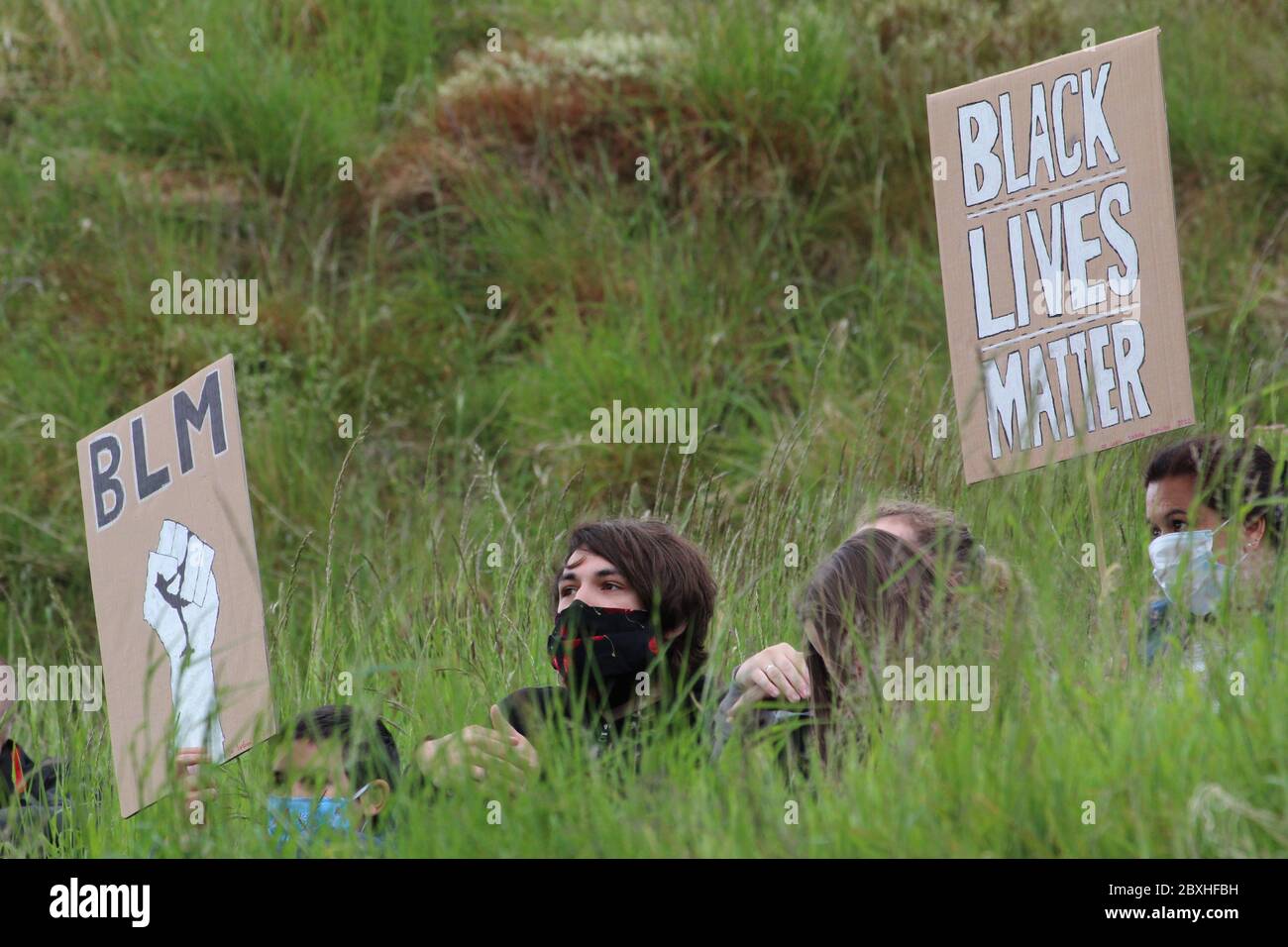 La gente que lleva una máscara sentada en hierba alta y sosteniendo los signos leyendo vidas negras importa en una demostración en Edimburgo Foto de stock