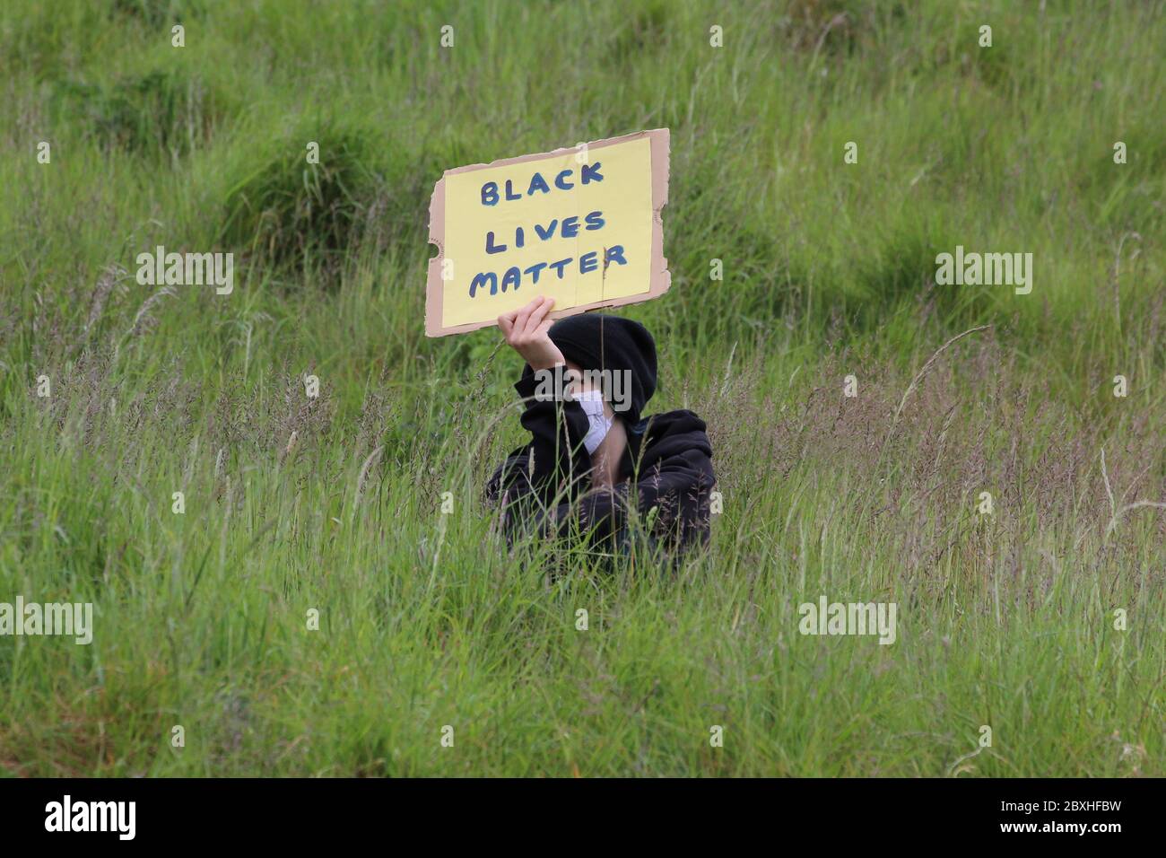 Un hombre con una máscara de cara sentado en hierba alta y sosteniendo un cartel leyendo vidas negras importa en una demostración en Edimburgo Foto de stock