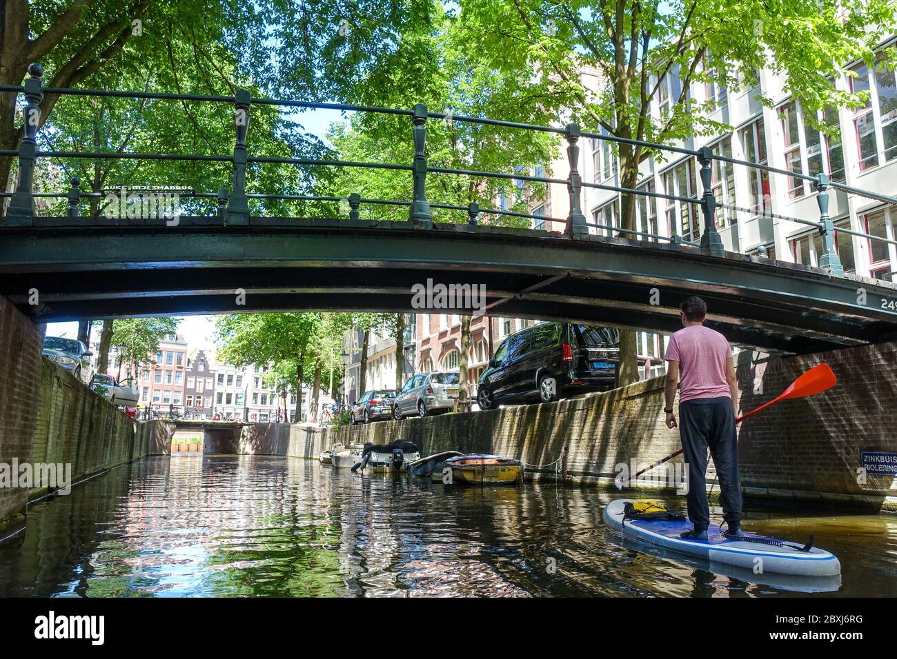 Hombre en un SUP (stand-up paddle board) en los canales en el centro de la tranquila Ámsterdam (países Bajos) durante la crisis de Covid-19 Foto de stock