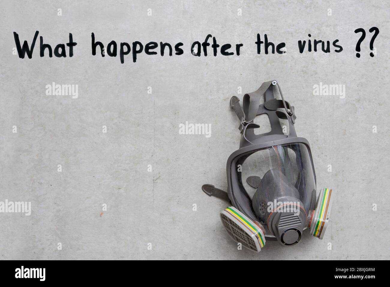Una máscara de gas cuelga en la pared de concreto y encima de ella está escrito, "Qué sucede después del virus". Foto de stock