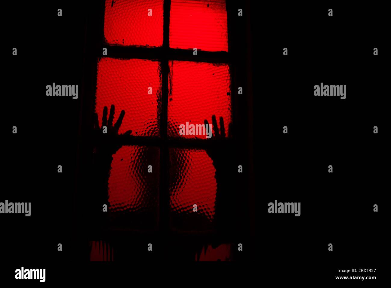 Una sihouette de miedo de la persona que se inclina contra la ventana en la oscuridad Foto de stock