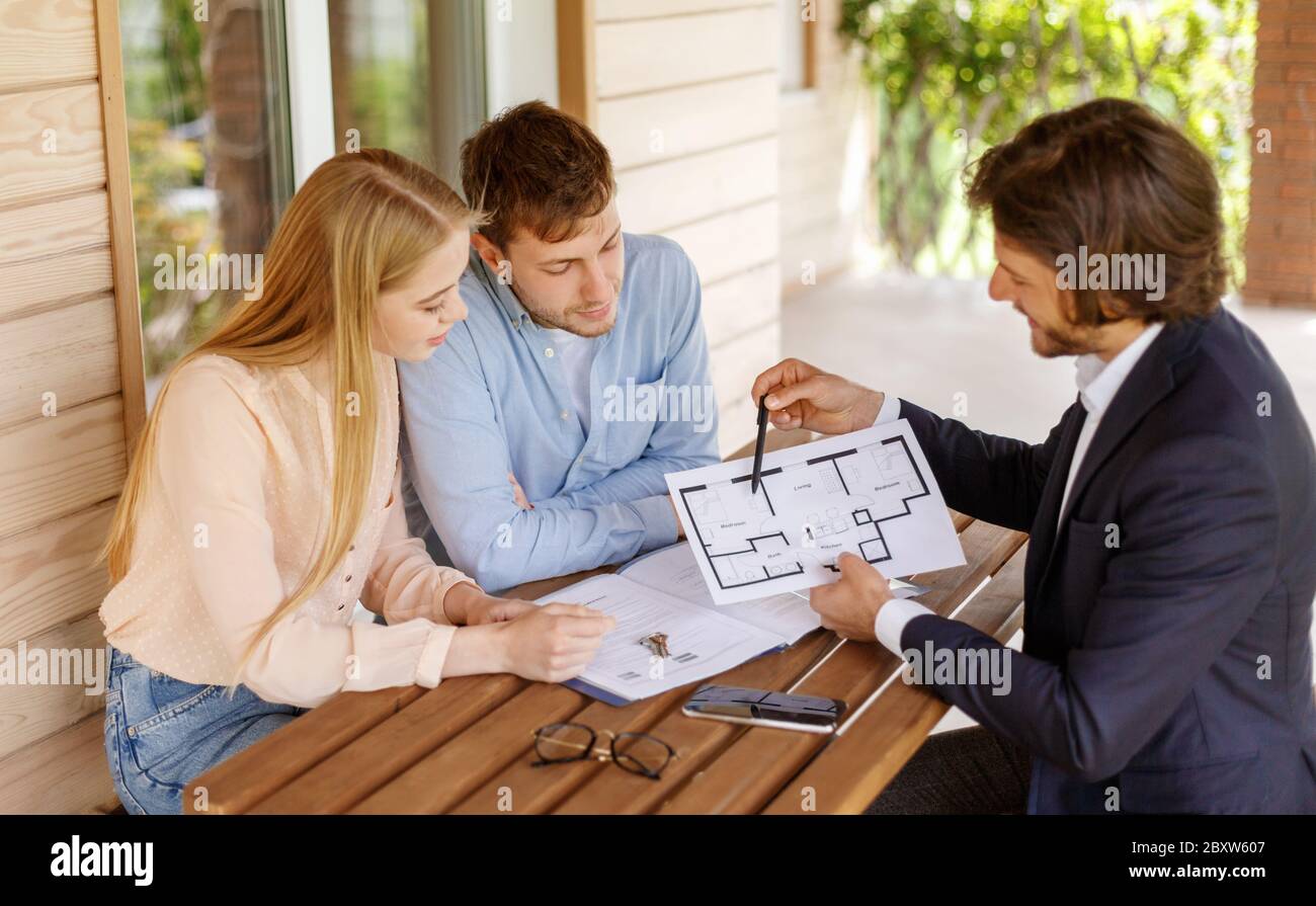 Agente inmobiliario mostrando el plan de la casa a la pareja milenaria en la mesa en el porche Foto de stock