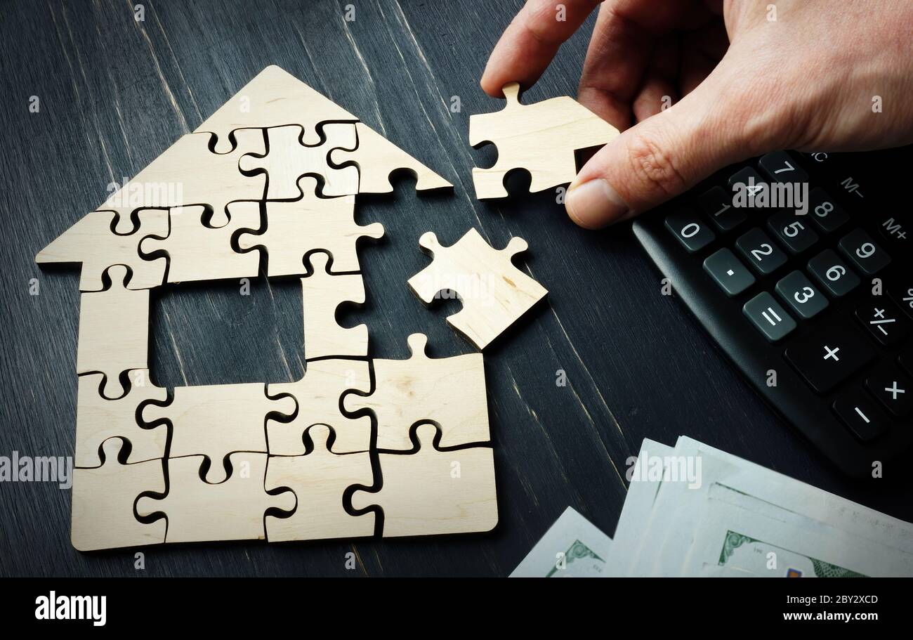 Ahorros en la compra de bienes raíces o una hipoteca. Una mano es recoger una casa de piezas de un rompecabezas. Foto de stock