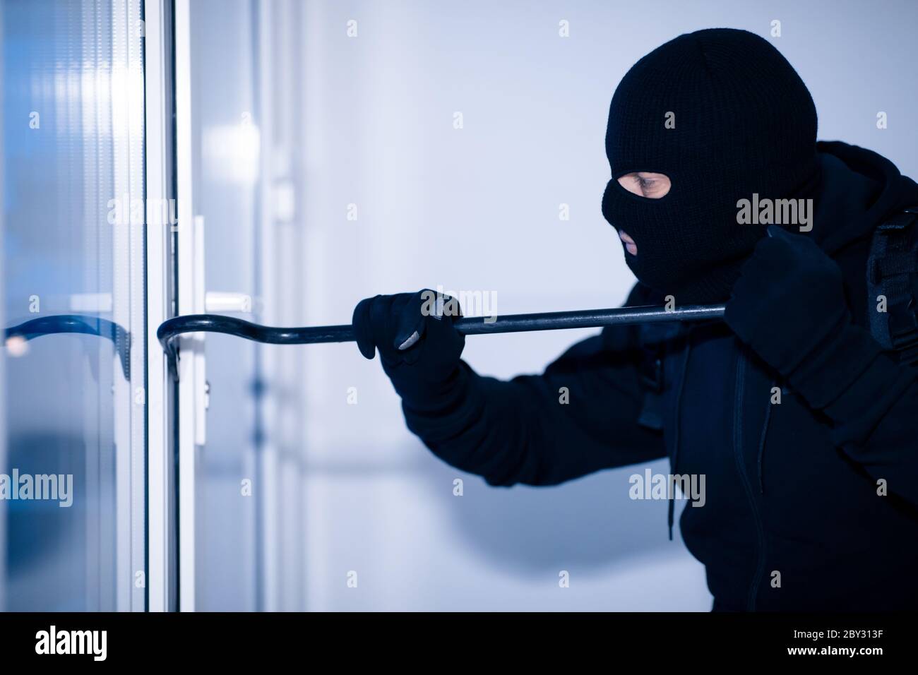 Ladrón en negro balaclava puerta de grietas con crowbar Foto de stock