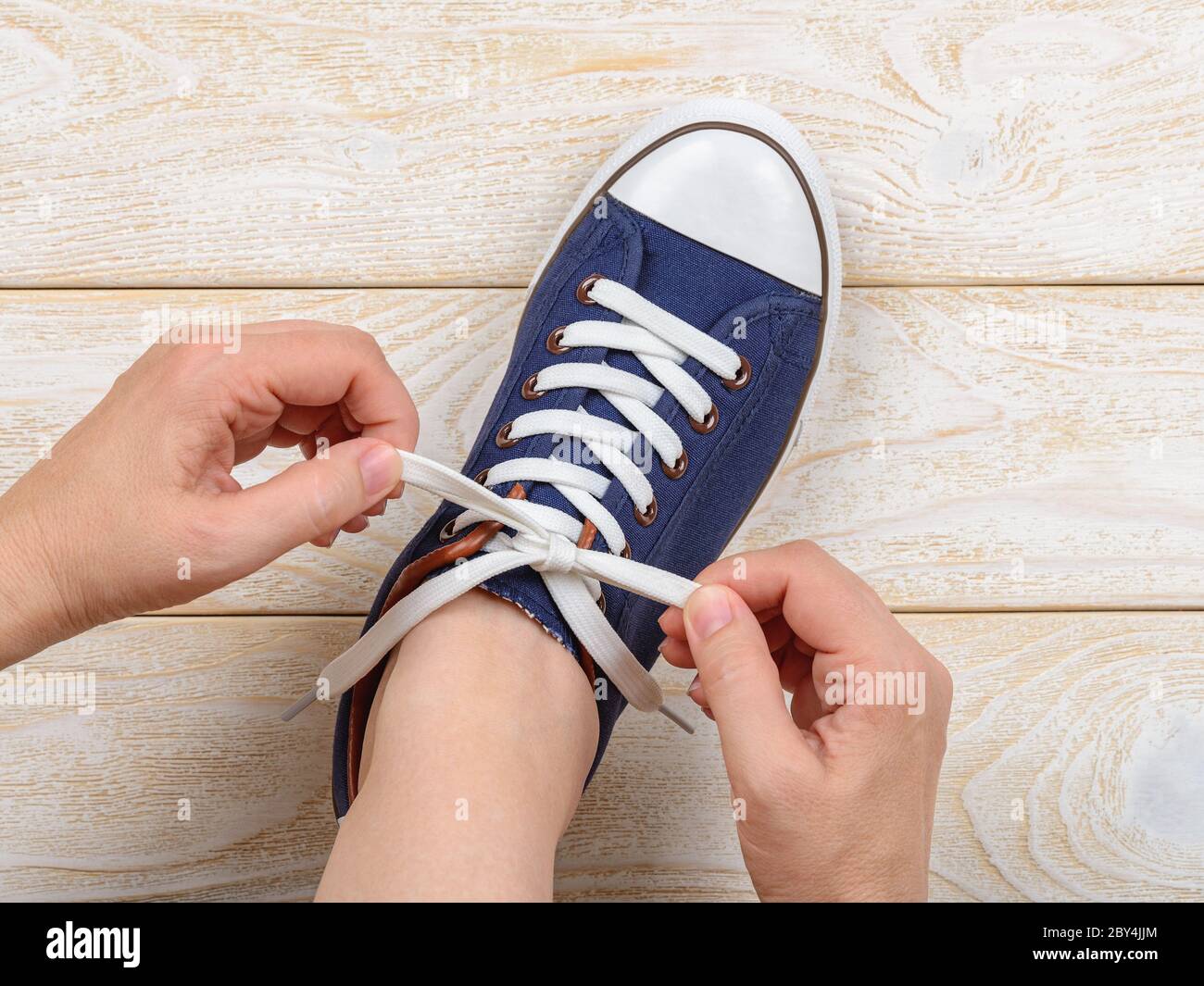 Las manos de la mujer caucásica atan cordones elásticos blancos en las  clásicas zapatillas de deporte o zapatillas de deporte de interior. Calzado  cómodo para hacer ejercicio y deporte. Zapatos con cordones