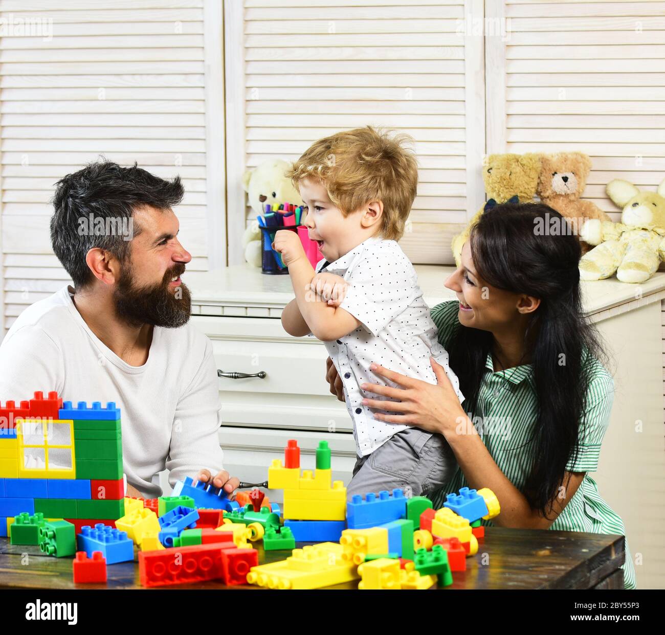 Mamá, papá y niño con juguetes sobre fondo de madera jugar con bloques de  plástico. La familia joven pasa tiempo en la sala de juegos. Concepto de  familia y niñez. Los padres