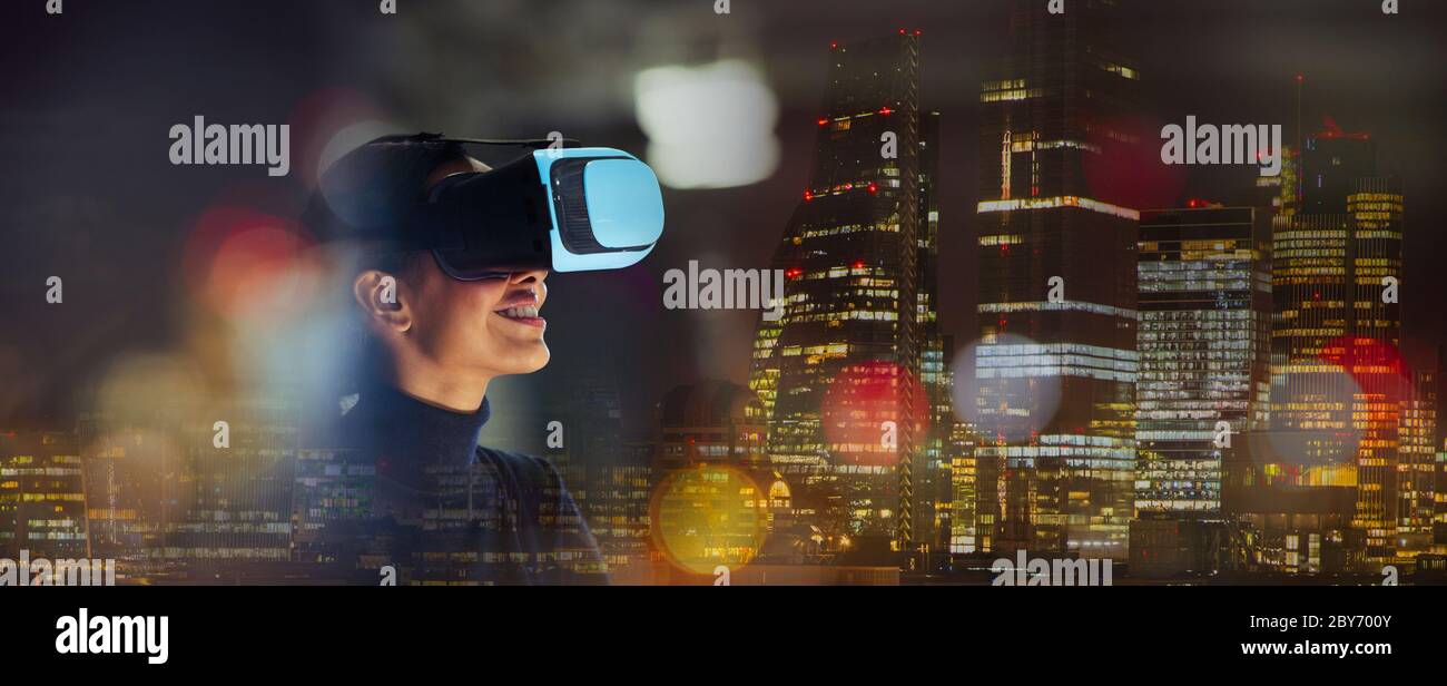 Mujer de negocios sonriente usando gafas de realidad virtual en la ciudad por la noche Foto de stock