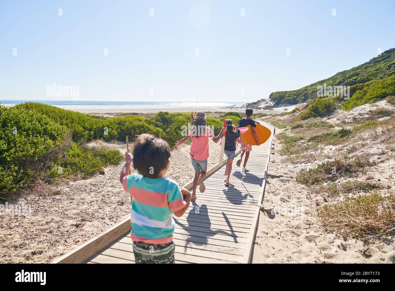 Hermanos y hermanas corriendo en el soleado paseo marítimo Foto de stock