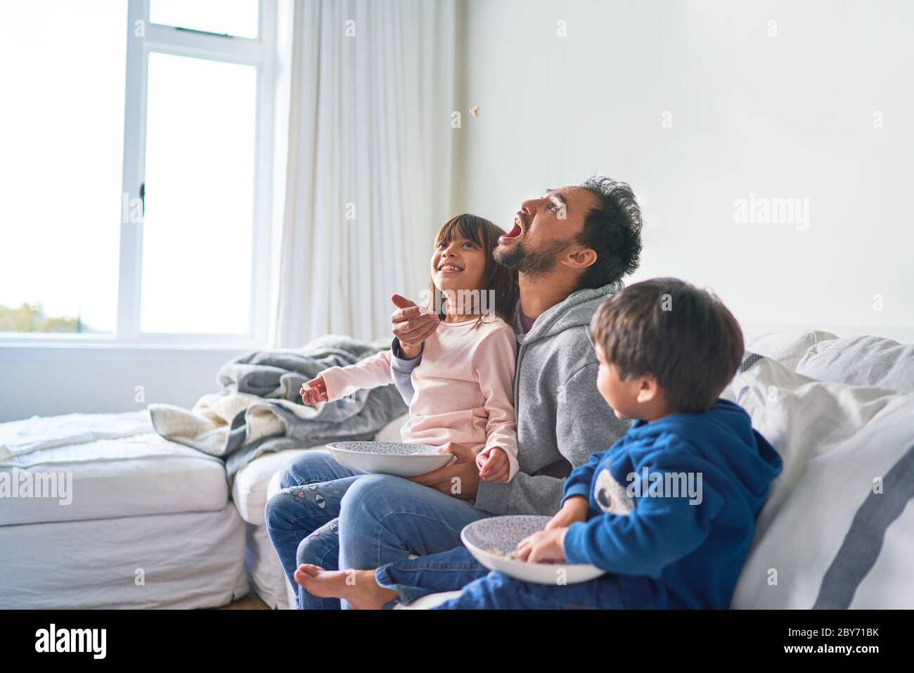 Familia juguetona comer palomitas en el sofá Foto de stock
