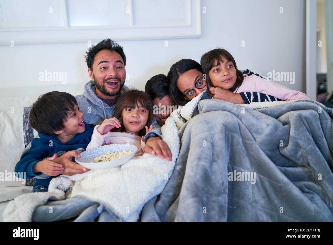 Familia acurrucada y viendo una película de miedo en el sofá Foto de stock