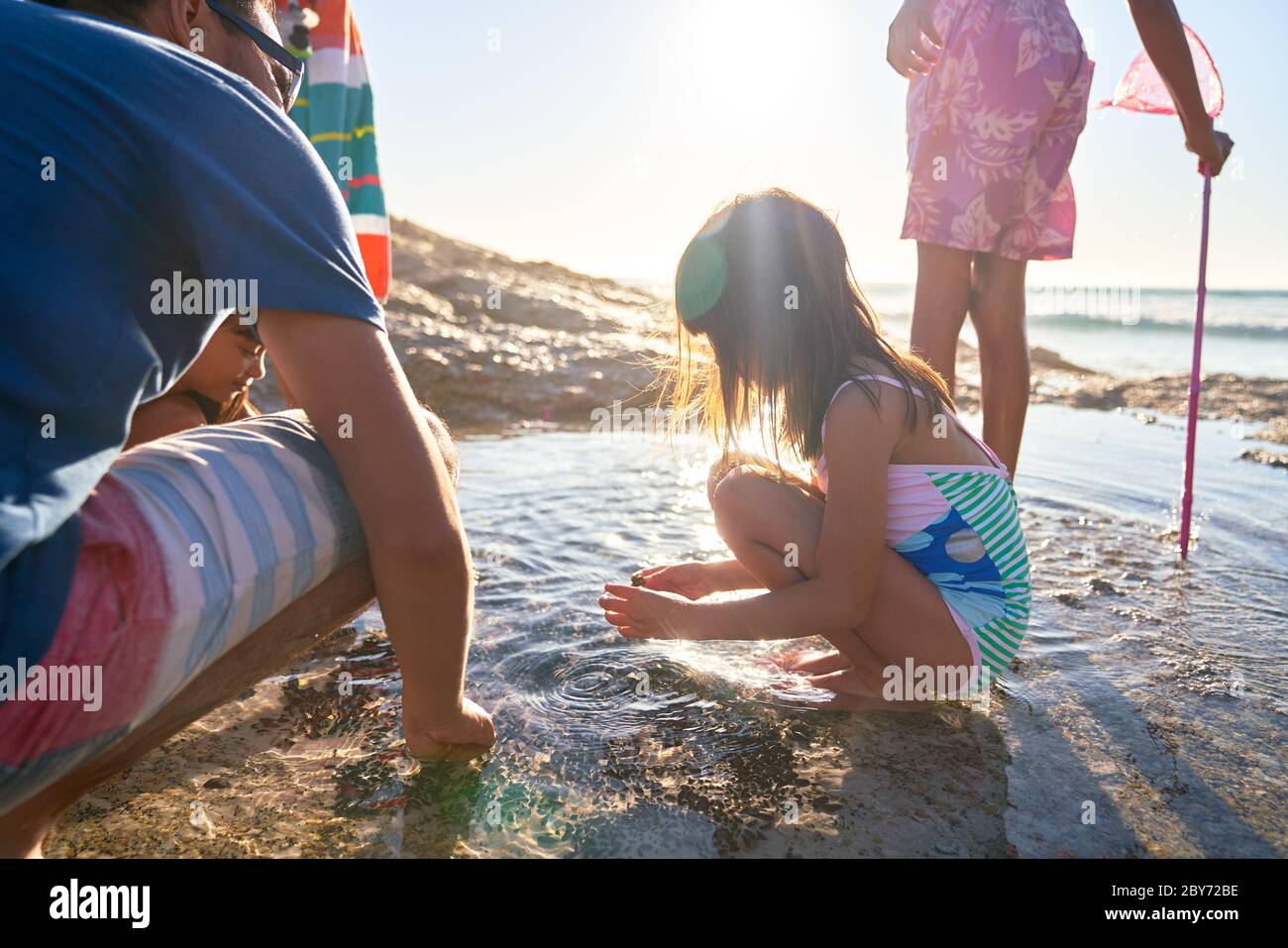 Familia jugando en piscina de marea en la playa soleada Foto de stock