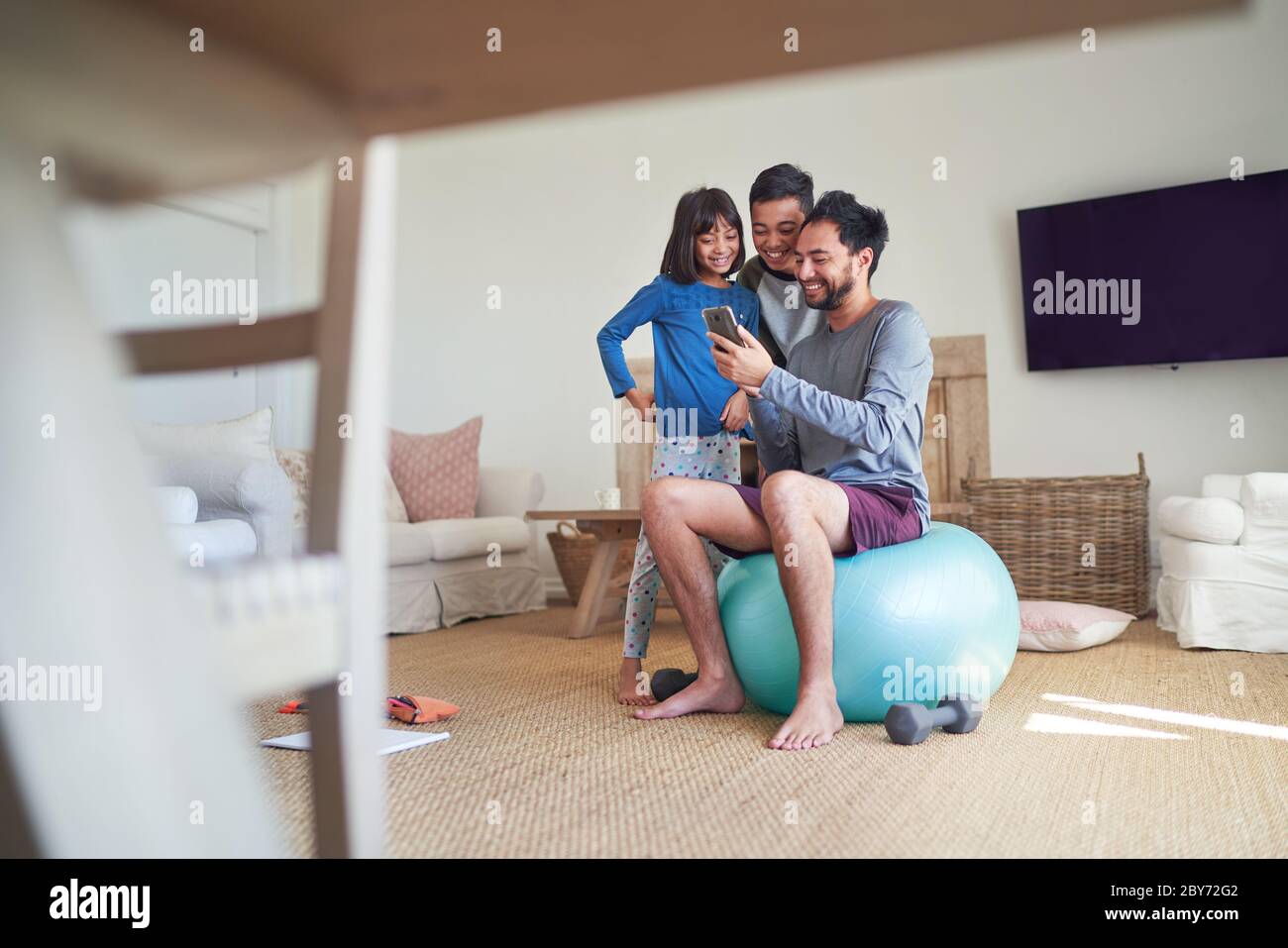 Padre y niños usando el teléfono inteligente y haciendo ejercicio en la sala de estar Foto de stock