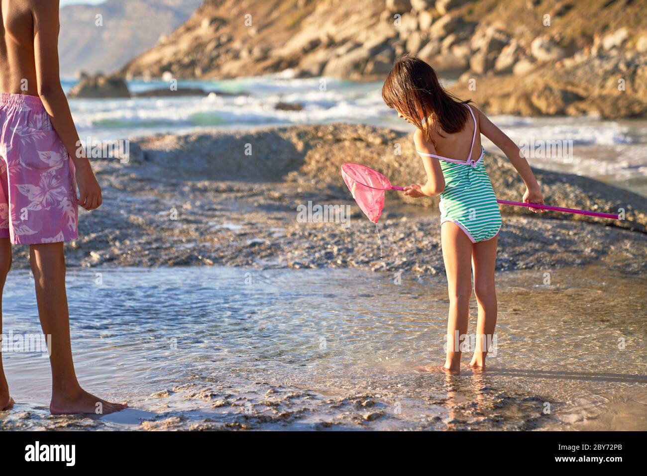 Chica con red de pesca jugando en piscina de marea en la playa soleada Foto de stock