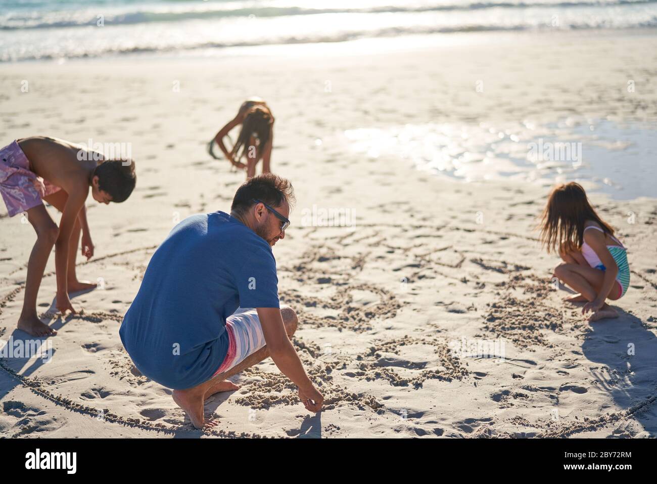 Familia dibujando en arena en la playa soleada Foto de stock