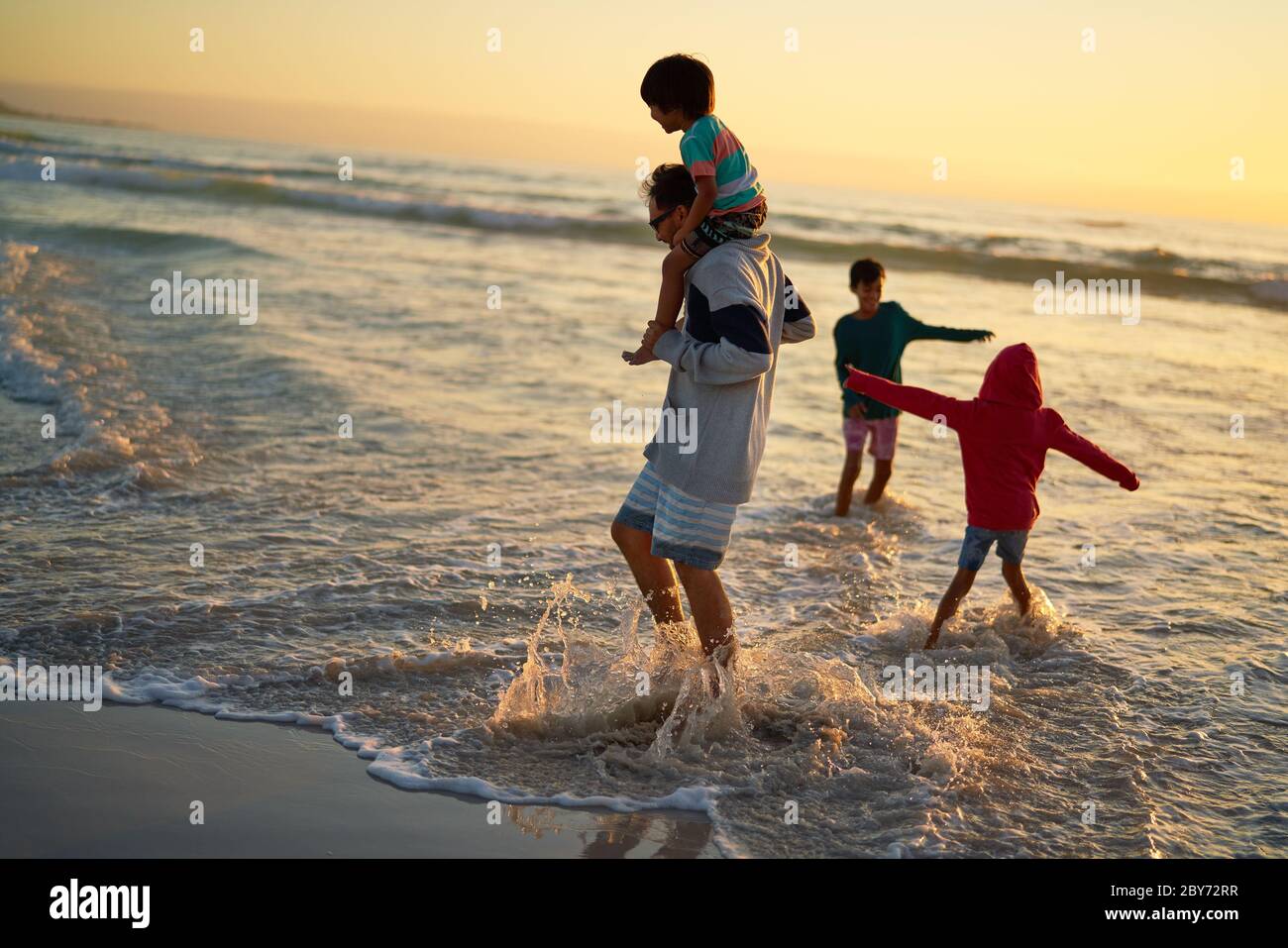 Chapoteo familiar y jugando en el surf del océano al atardecer Foto de stock