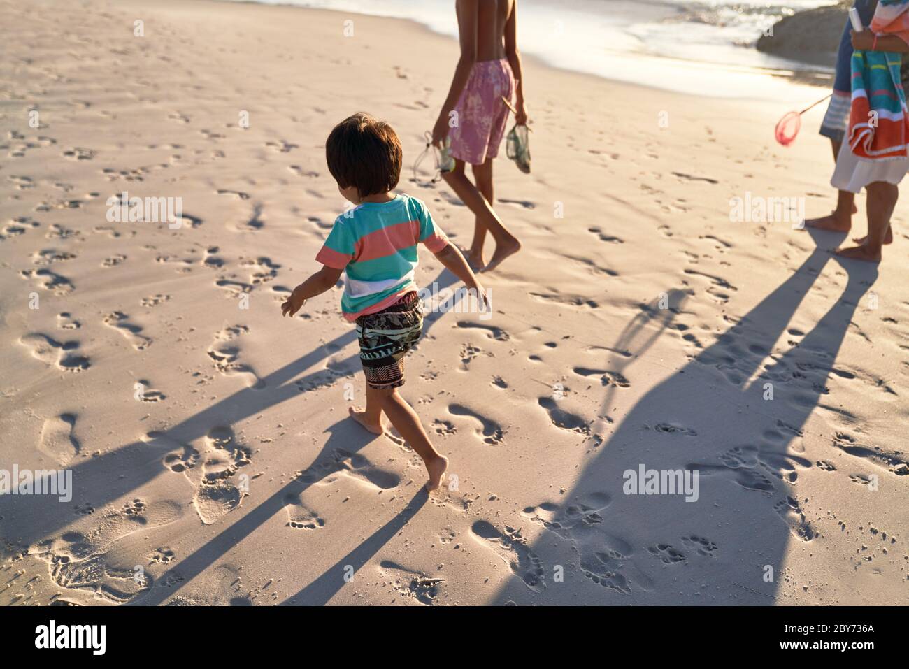 Lindo chico corriendo en la playa con la familia Foto de stock