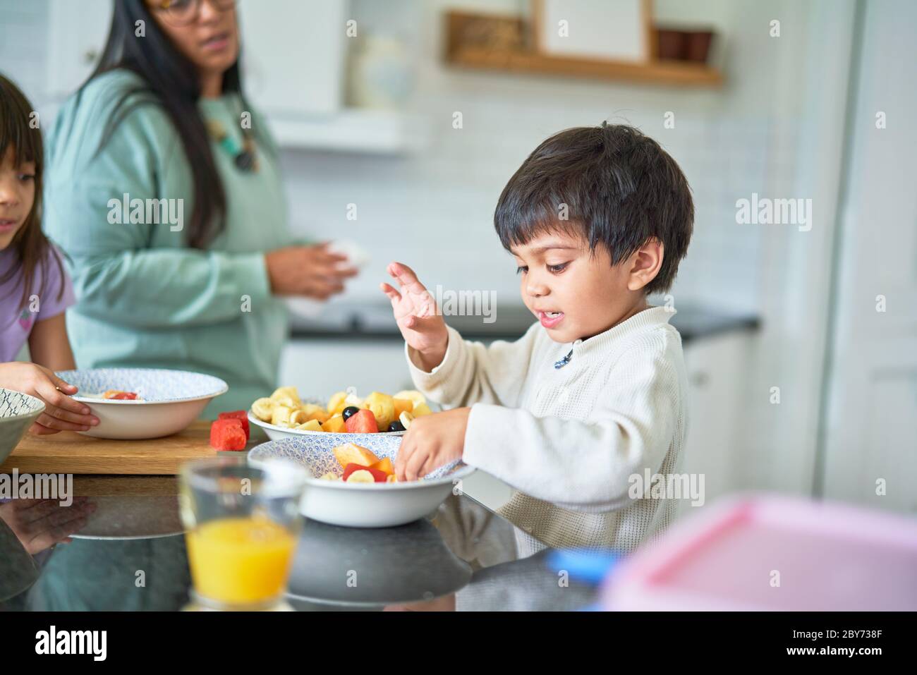 Lindo chico comiendo fruta fresca en la cocina Foto de stock