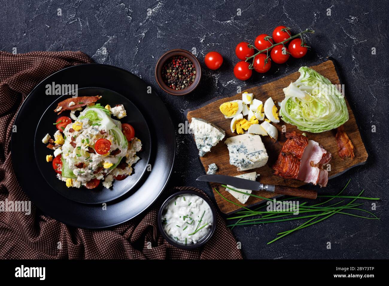 ensalada de cuña de iceberg cubierta con aderezo de queso azul, tocino frito crujiente, tomates cherry, huevos duros desmenuzados, cebolletas en platos negros en un conc Foto de stock