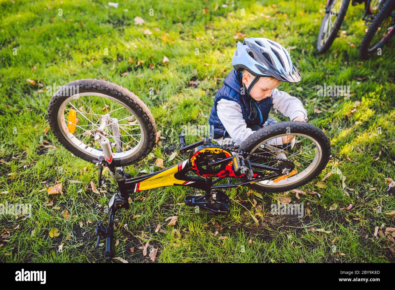 Ocio activo para niños en el parque. Un niño está estudiando el mecanismo  de una bicicleta de montaña. Niño arreglando una bicicleta en el bosque.  Ciclismo club para Fotografía de stock -