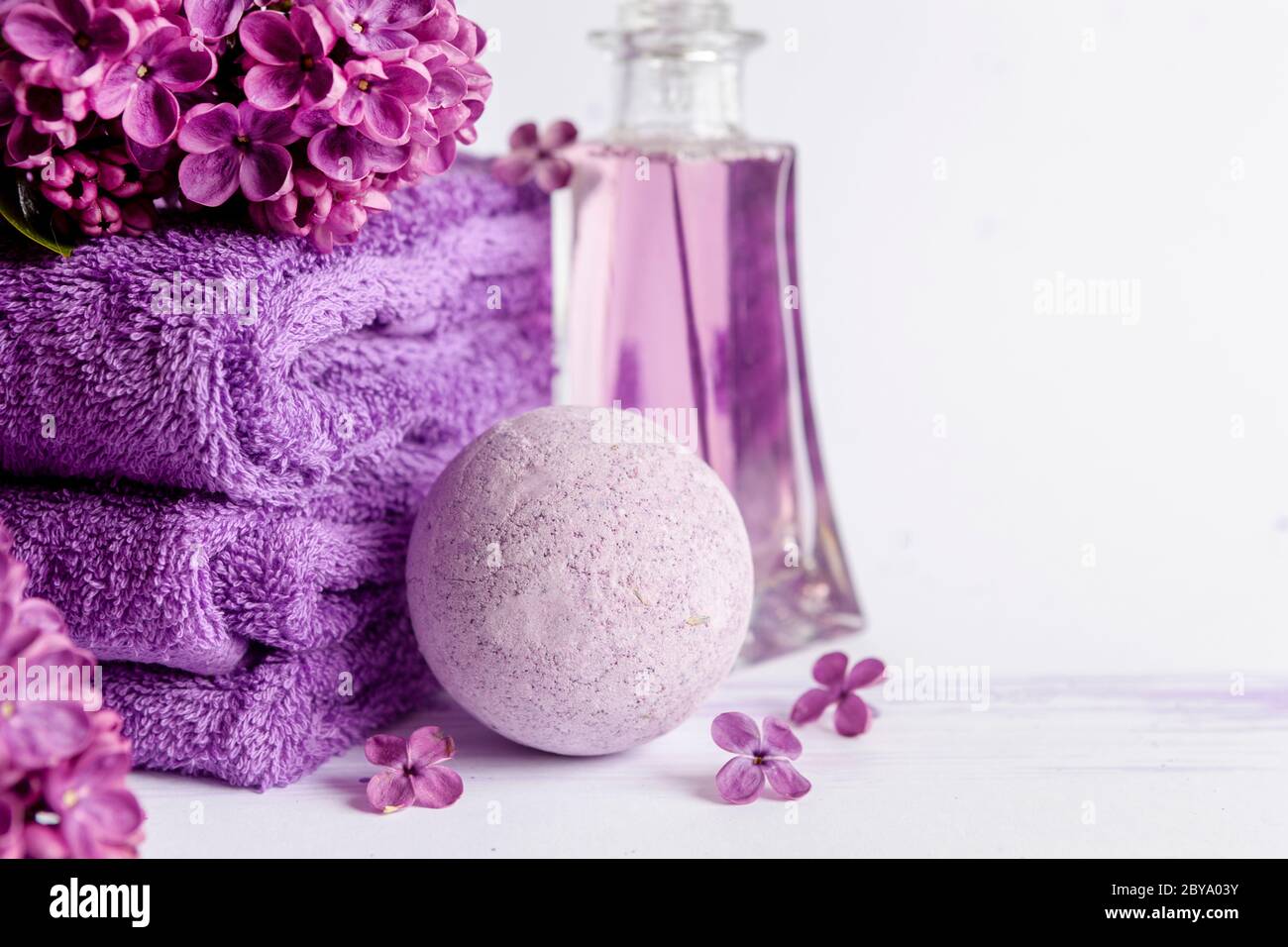 Flores lilas, bulbo aromático de sal marina, perfume púrpura y toallas.  Concepto de spa, salón de belleza y salud, tienda de cosméticos. Foto de  primer plano en blanco Fotografía de stock -