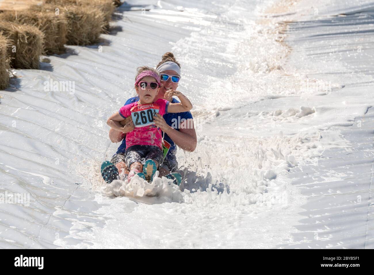 Poley Mountain, New Brunswick, Canadá - 10 de junio de 2017: Participando en la recaudación de fondos anual 'Mud Run for Heart'. Una mujer y un niño se deslizan por una espuma Foto de stock