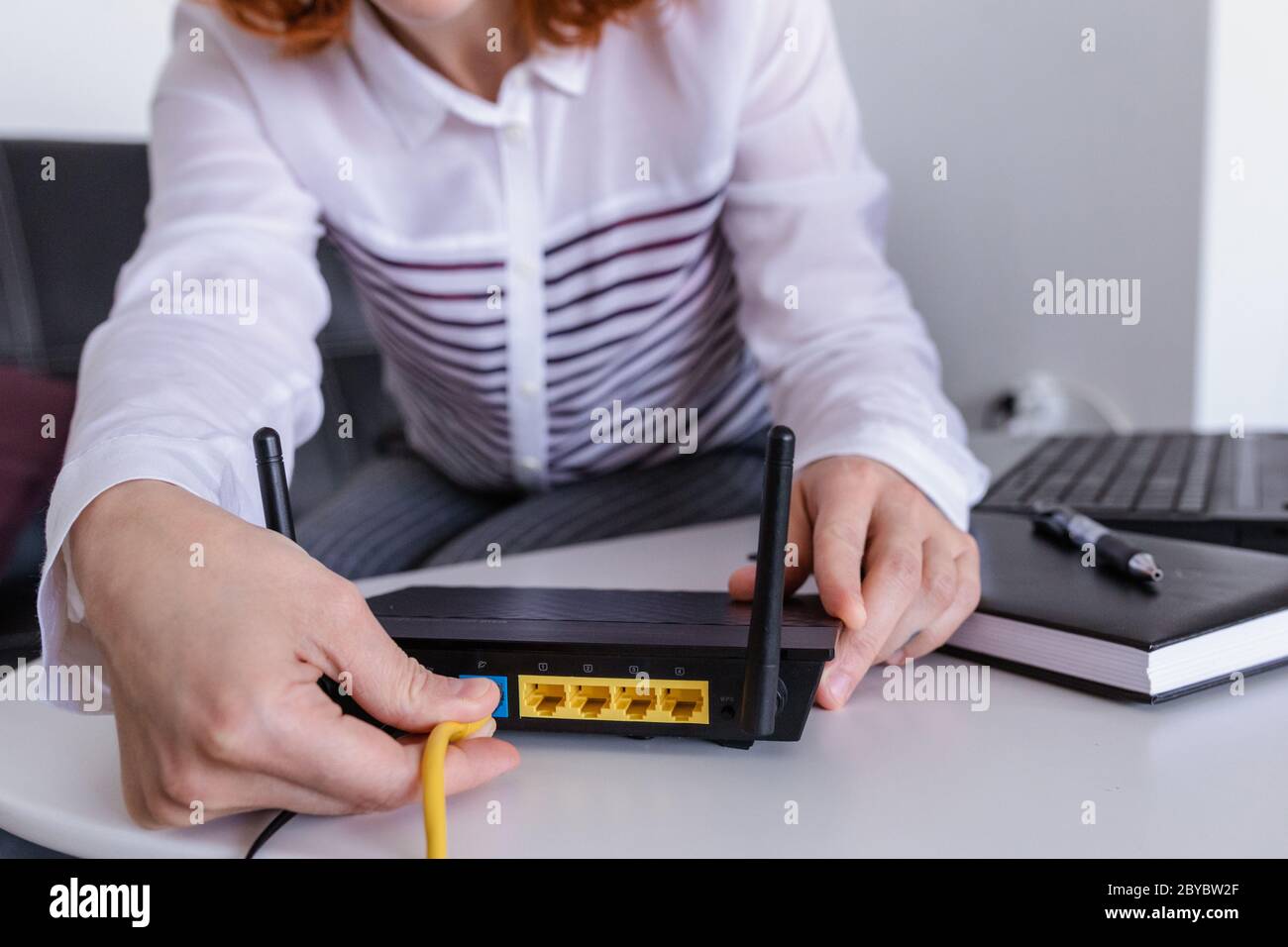 Redhead Woman conecta el cable de Internet a la toma del router. Concepto de Internet rápido e inalámbrico Foto de stock