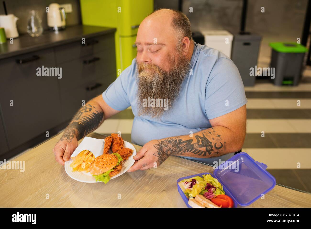 Hombre gordo feliz con tatuajes tomando plato con hamburguesa Foto de stock