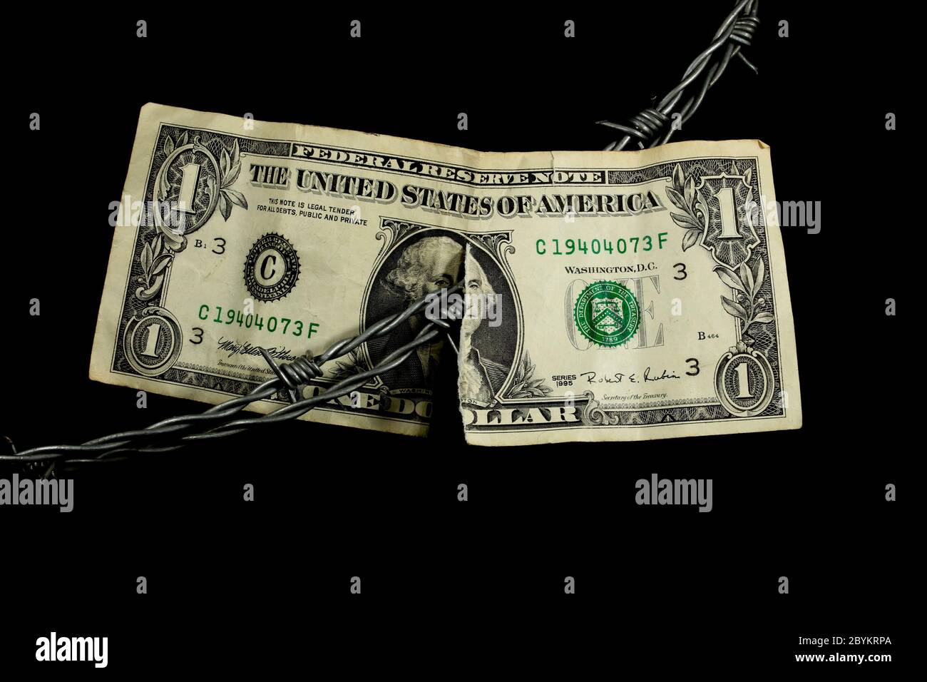 Alambre de púas que divide una vieja factura de dólar desgastada y rasgada Foto de stock